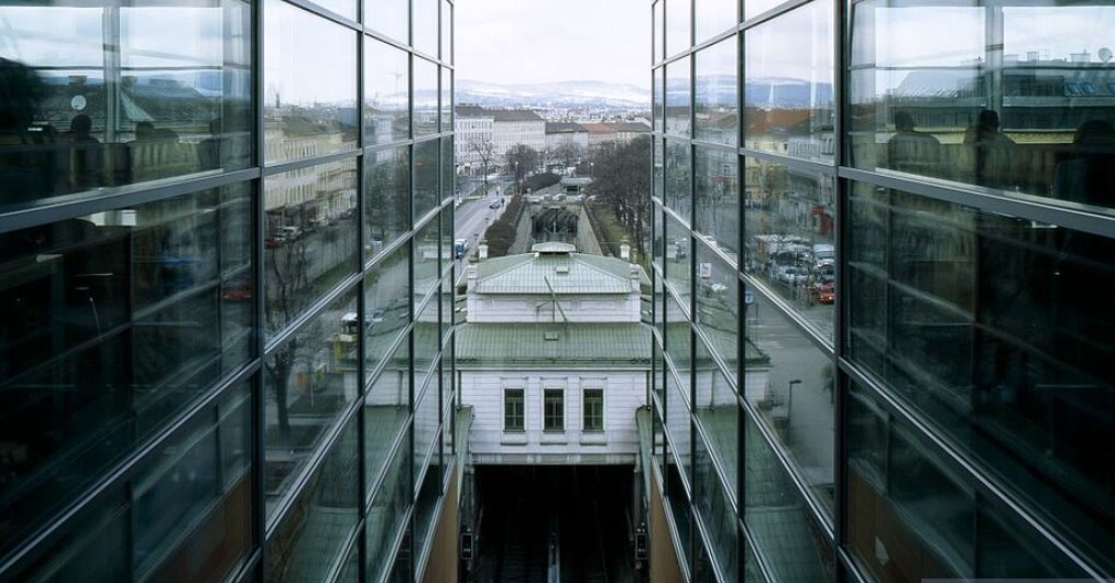 Das Bild zeigt den Blick aus dem Fenster der Hauptbücherei Wien. Neben zwei verglasten Wänden sieht man dazwischen eine U-Bahn Station