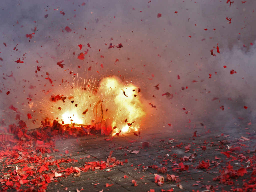 ein Feuerwerk explodiert am Boden. Rotes Feuerwerksmaterial liegt am Boden und fliegt in der Luft
