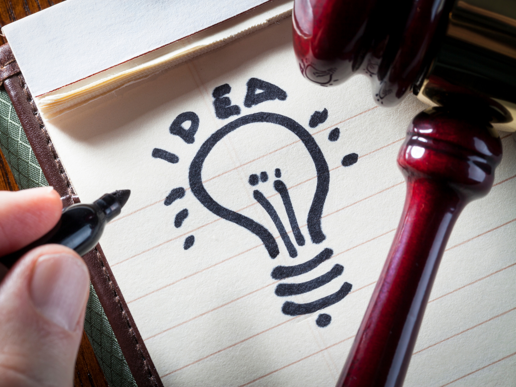 ein Richterhammer liegt neben einer gezeichneten Glühbirne über der "idea" geschrieben steht 