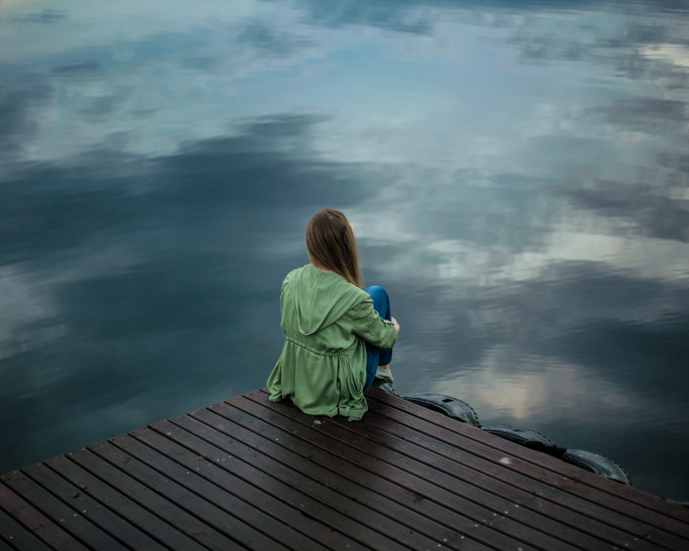 eine Person sitzt alleine auf einem Steg vor Wasser