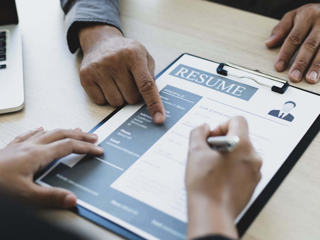 Am Tisch liegt ein Bewerbungsschreiben. Man sieht Hände von zwei Personen die auf das Bewerbungsschreiben zeigen und etwas ausbessern.