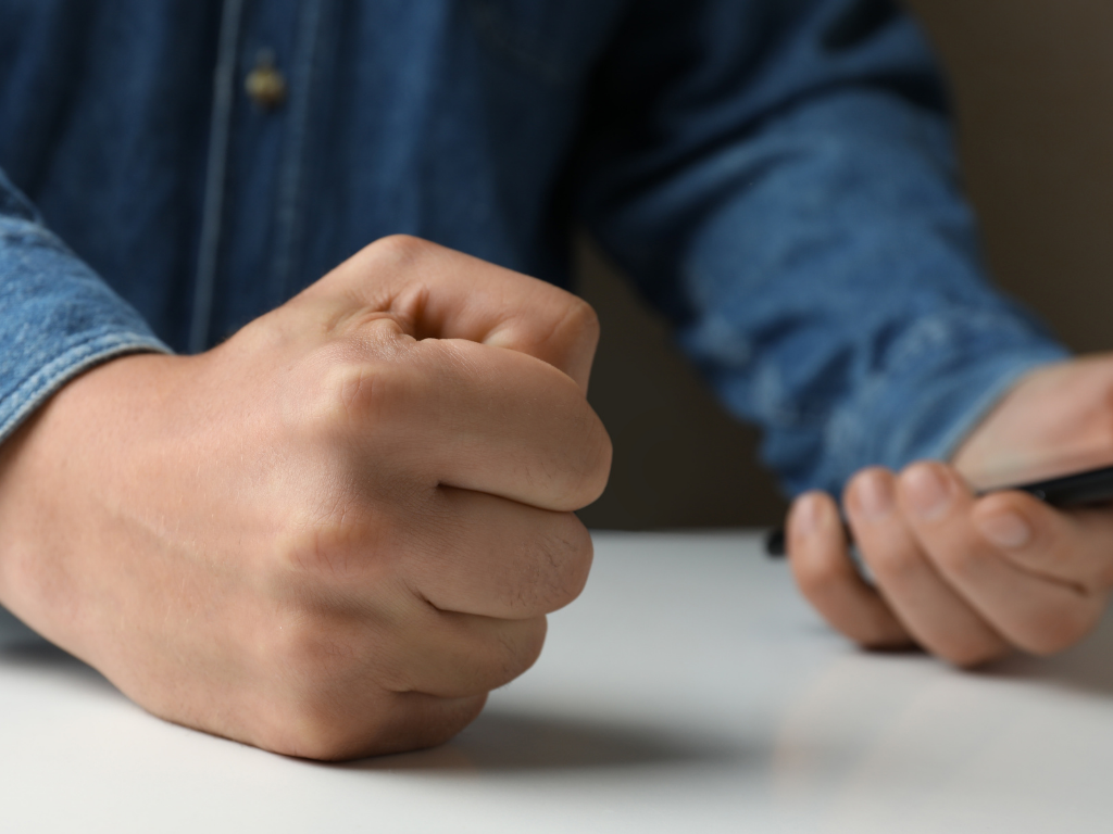 Mann schaut auf sein Handy und ballt die Faust. Nur die Arme am Tisch sind zu sehen