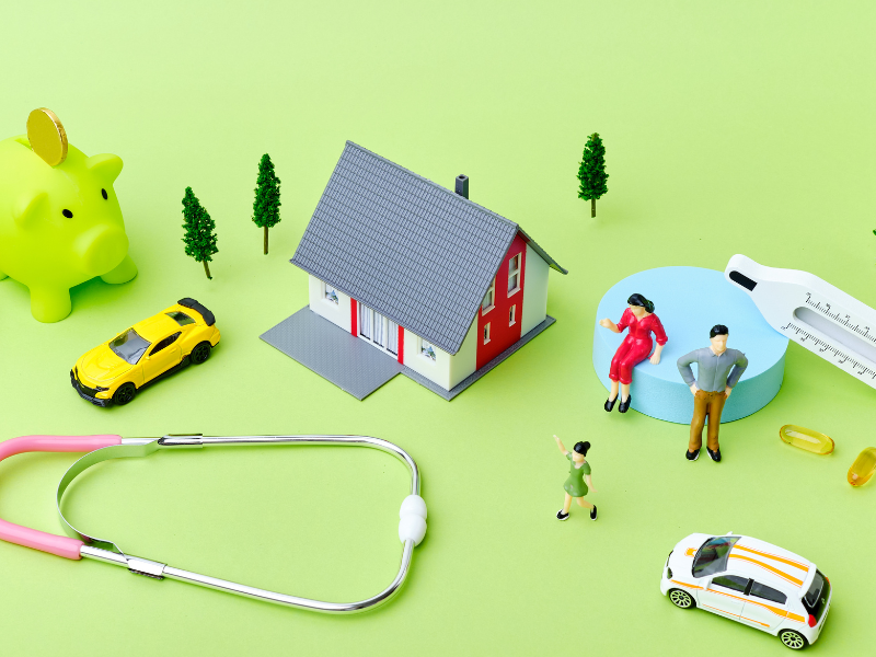 Ein grüner Hintergrund, davor ein Haus, ein Sparschwein, ein Auto und Gesundheitsutensilien 