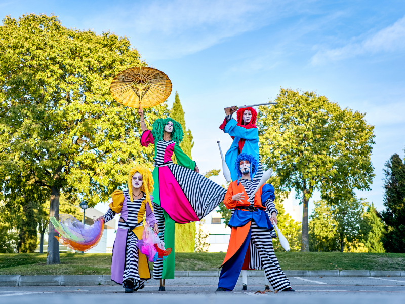Das Bild zeigt eine Gruppe von vier farbenfroh kostümierten Straßenkünstlern, die unter freiem Himmel posieren.