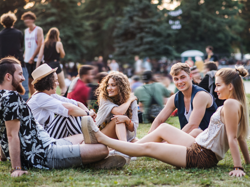 Das Bild zeigt eine Gruppe junger Erwachsener in einer sommerlichen, entspannten Festival-Atmosphäre