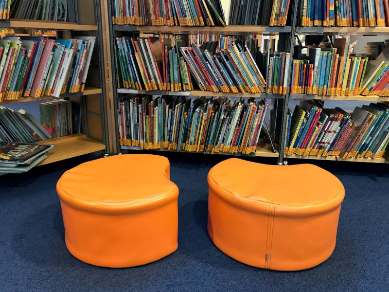 Zwei orangene Sitzhocker vor einer Bücherwand.