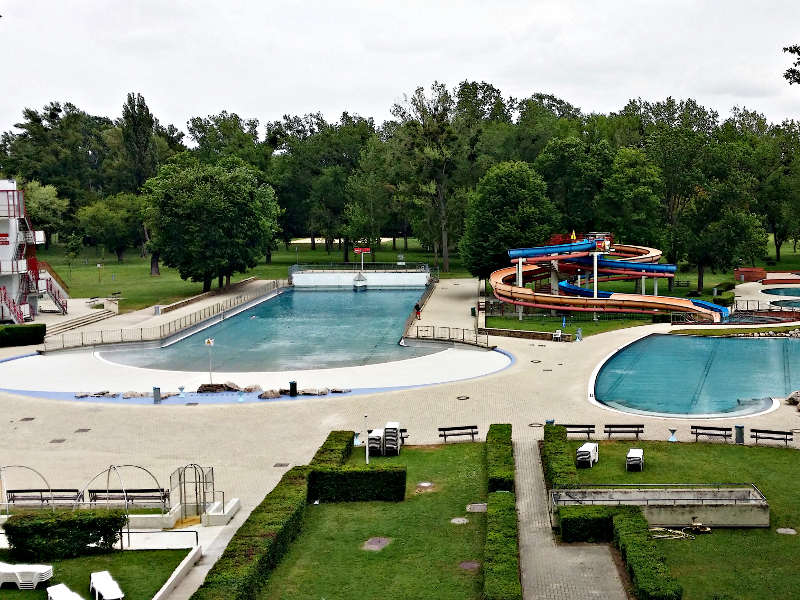 Stadionbad Zwei Wasserbecken, zum rechten führen eine blaue und orangene Rutsche herunter, welche ineinander verdreht sind.