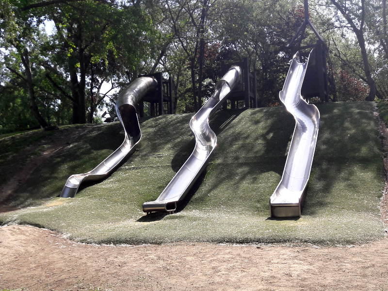 Donaupark Ein mit Rasenteppich überzogener Hügel, von dem drei Metallrutschen in Blitzform herunter gehen.