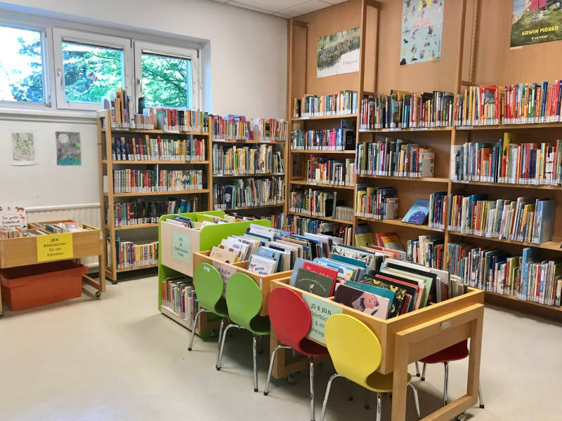 Kinderbereich Mehrere Bücherregale und Holzkisten gefüllt mit Kinderbüchern. Vor den Holzkisten stehen bunte Sessel.