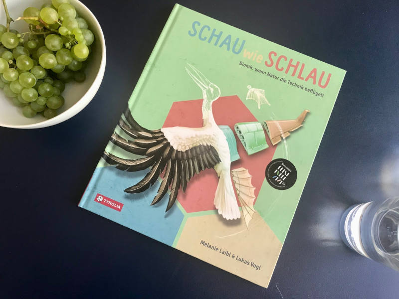 Schau wie schlau Kinderbuch auif einem Tisch, daneben Trauben und ein Glas Wasser