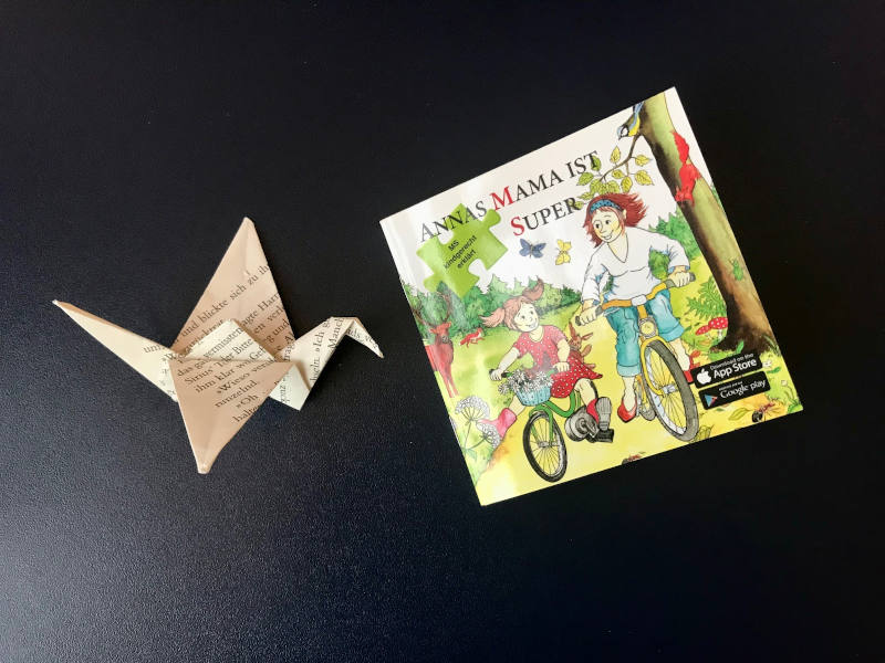 Buch "Annas Mama ist super" von Sabina Dirnberger und Renate Magerl, daneben ein Papierkranich.