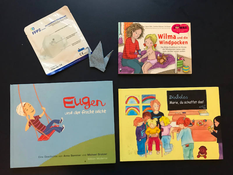 Bücher Wilma und die Windpocken, Eugen und der freche Wicht sowie Diabetes: Marie, du schaffst das, daneben ein Papierkranich und eine FFP2-Maske.