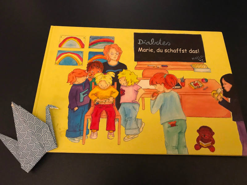 Buch "Diabetes: Marie, du schaffst das!" von Christine Jüngling und Dilan Besak, daneben ein Papierkranich.
