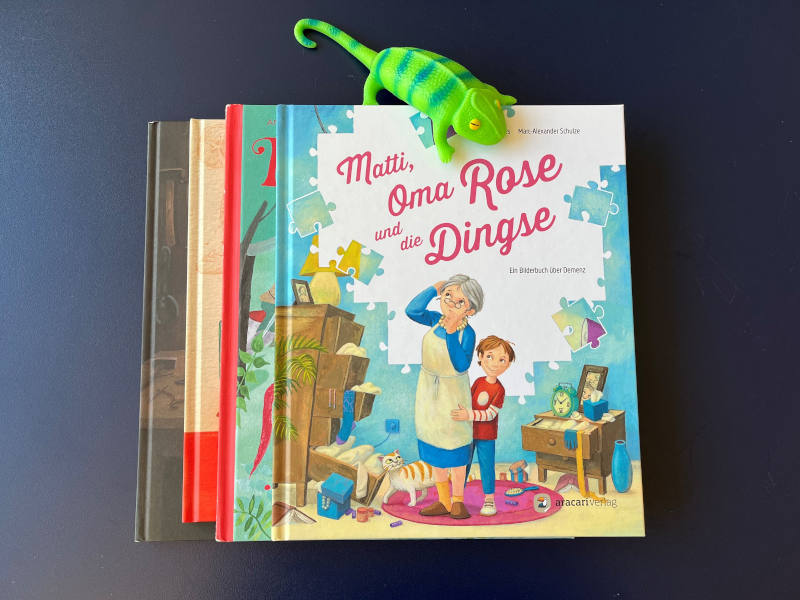 Bücherstapel, ganz oben liegt "Matti, Oma und die Dingse" von Brigitte Endres und Marc-Alexander Schulze. Über dem Bücherstapel ist ein Stoffchamäleon.. 