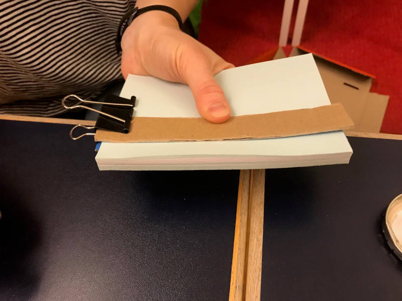 Papierstapel zwischen zwei Kartonstreifen wird mit einer Klammern fixiert.