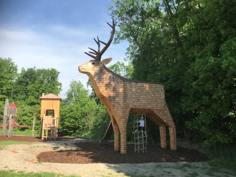 Riesen-Holzhirsch mit Rutsche. Im Hintergrund ein Kletterturm.