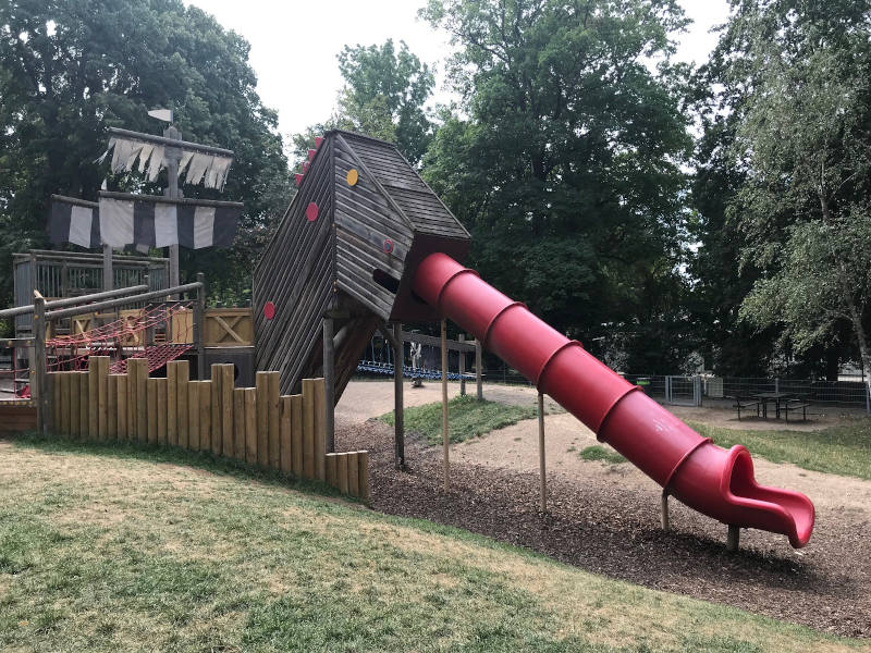 Ein Holzschiff, von dem eine rote Rutsche runter geht. 