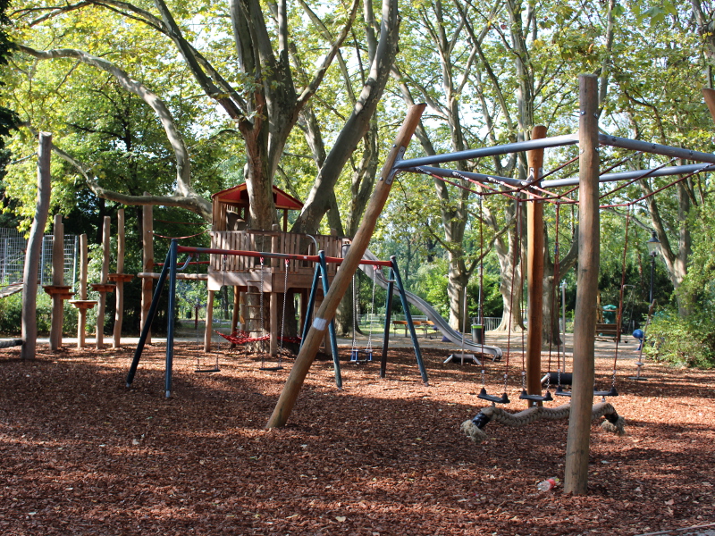 Blick auf den Spielplatz mit Schaukeln im Vordergrund und einem Klettergerüst im Hintergrund