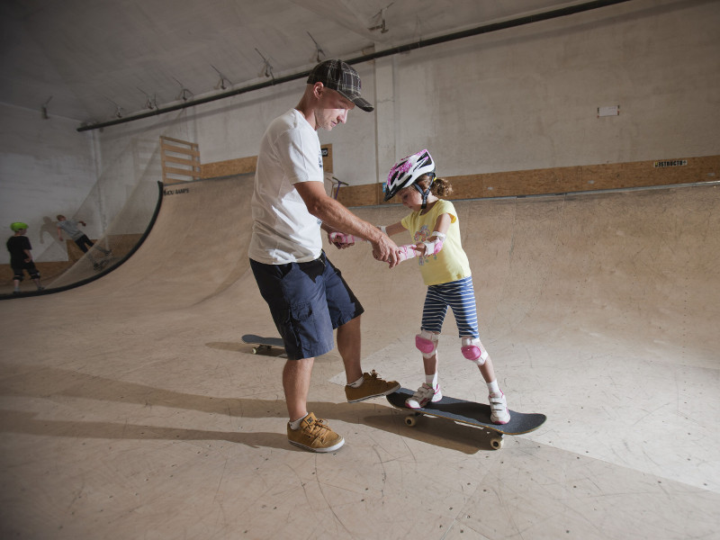 Erwachsener hilft Kind mit Skateboard