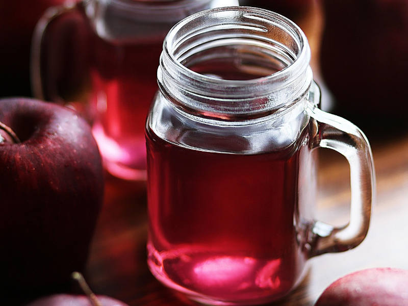 Glas mit rotem Saft, daneben liegt ein roter Apfel