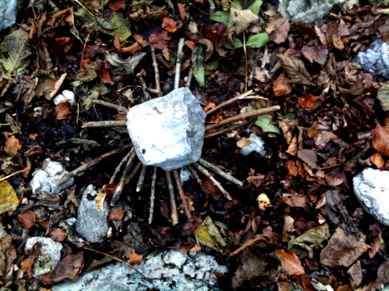 Hlozstäbchen im einem Kreis gelegt auf herbstlich verfärbten Blättern mit einem Stein in der Mitte