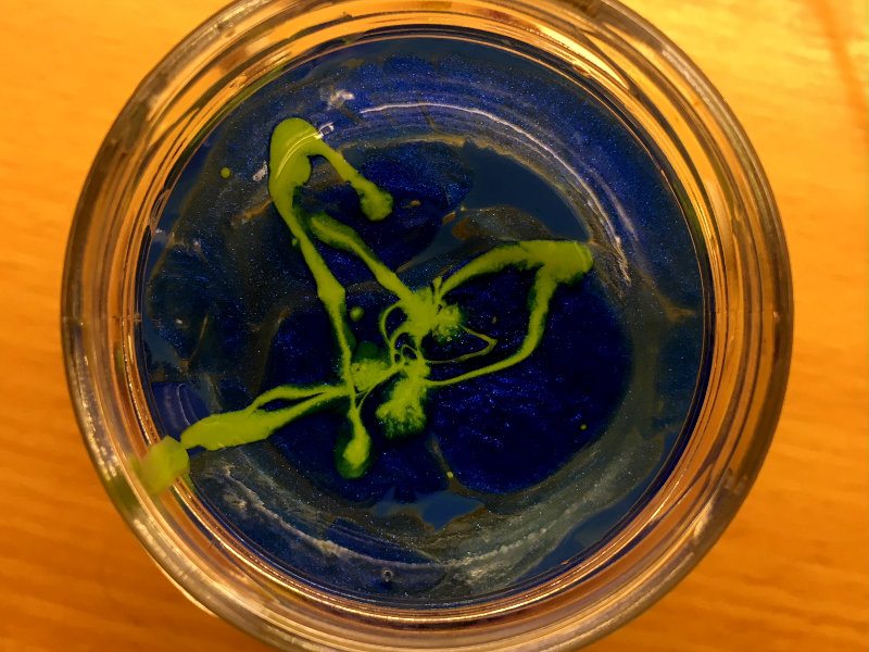 In dem Bild sieht man ein Glas Wasser, in das zwei verschiedene Nagellacke auf der Wasseroberfläche schimmen. Mit dieser Basis werden im nächsten Schritt die Ostereier marmoriert