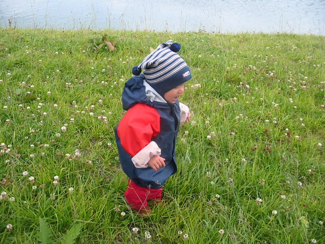 Kleinkind in Regenoutfit auf Wiese