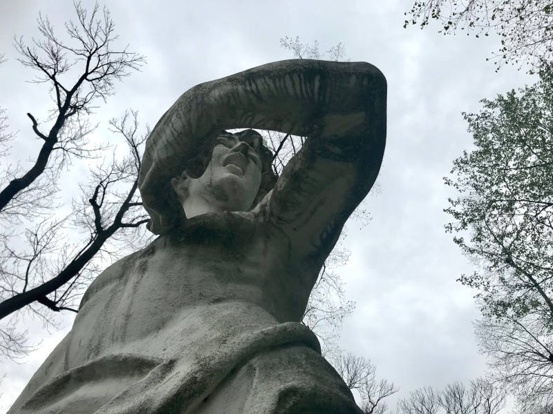 Statue von unten rauf fotografiert. Das Gesicht ist verzerrt, der Mund offen, die Hand berührt die Brust, der Ellenbogen ist vom Körper weggestreckt.