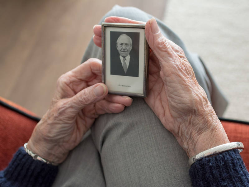 Nahaufnahme von älteren Händen, die ein eingerahmtes schwarz-weiß Portrait halten.
