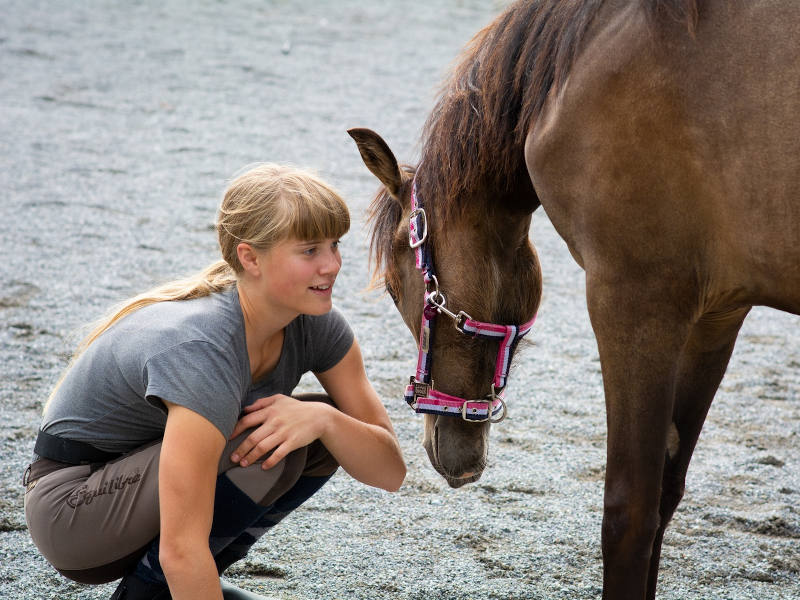 Kind im Reitdress kniet vor einem Pferd
