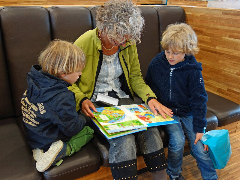 alte Frau sitzt mit einem Bilderbuch zwischen zwei Kindern