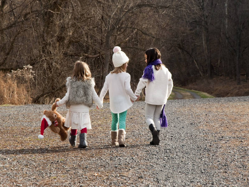 Kinder im Herbst drei Kinder von hinten, die sich an den Händen halten auf einer Schotterstraße