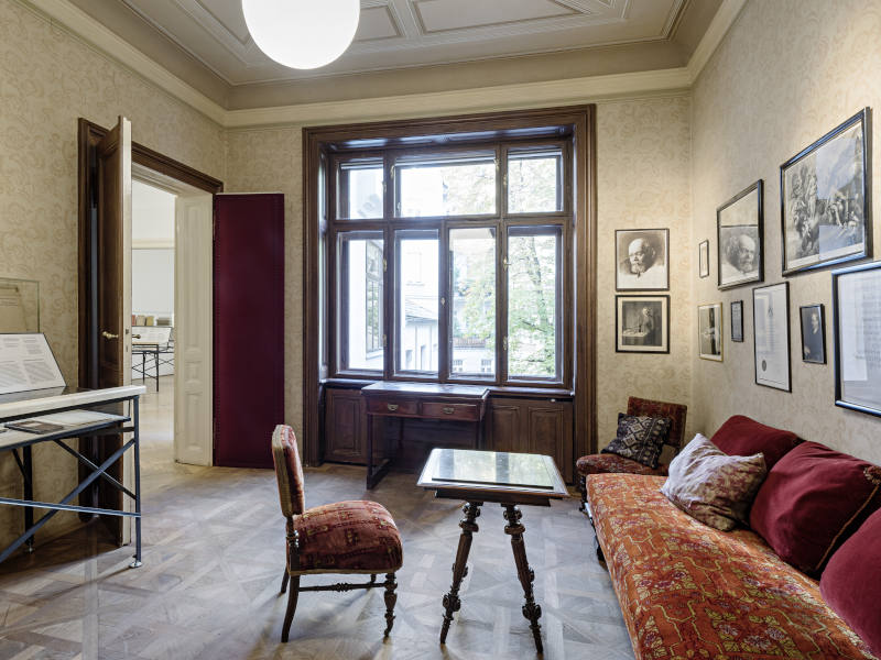 Wartezimmer im Freud Museum ein Sessel, ein Tisch und eine rot gepolsterte Bank, an den Wänden hängen Bilder