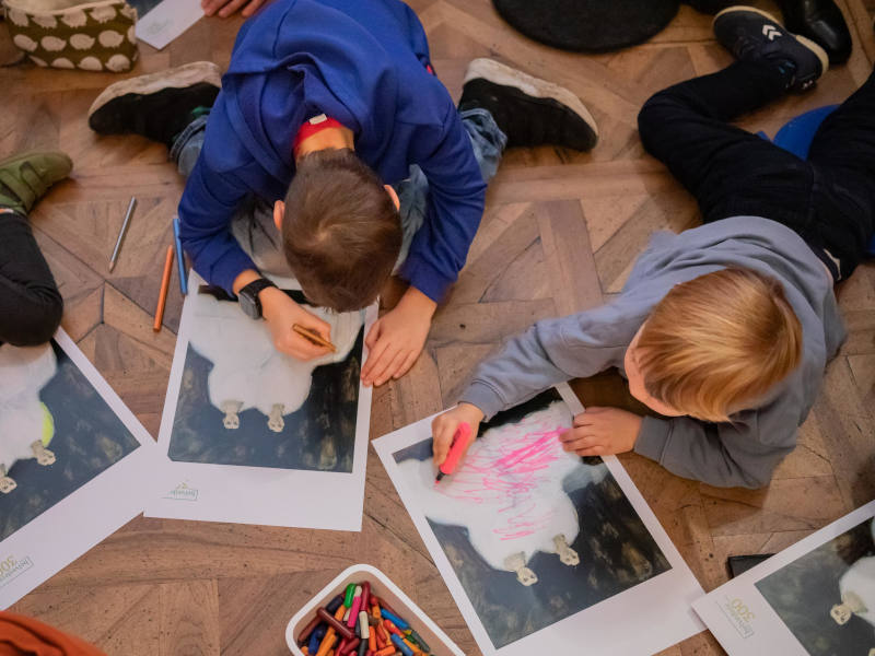 Kinder die am Holzboden sitzen/liegen und malen.