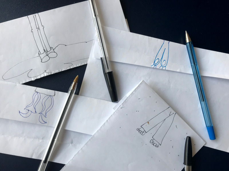 Beine gezeichnet beim Knickzeichenspiel. Zu sehen sind Beine die auf ein Papier gemalt sind. daneben liegt neben jedem Zettel ein Stift