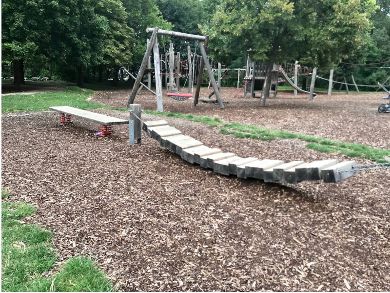 Balanciergeräte: Ein Holzbrett auf vier roten Spiralen und anschließend eine Holzbrücke: Mehrere Holzscheite aneinandergereiht, auf zwei Metallketten aufgefädelt, fixiert an zwei Holzpfeilern.