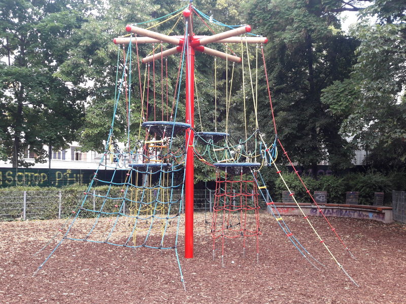 Kletterspinne: Großer roter Mast in der Mitte, ganz oben ein sechsarmiger Stern aus Holz von welchem Schnüre nach unten gespannt sind, über welche man durch Leitern und Plastikstücke nach oben und dazwischen herum klettern kann. Dazwischen sind vier Nestschaukeln angebracht.