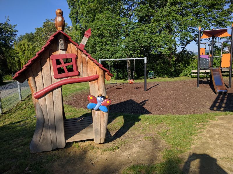 Spielhäuschen mit Schaukeln und Klettergerät im Hintergund