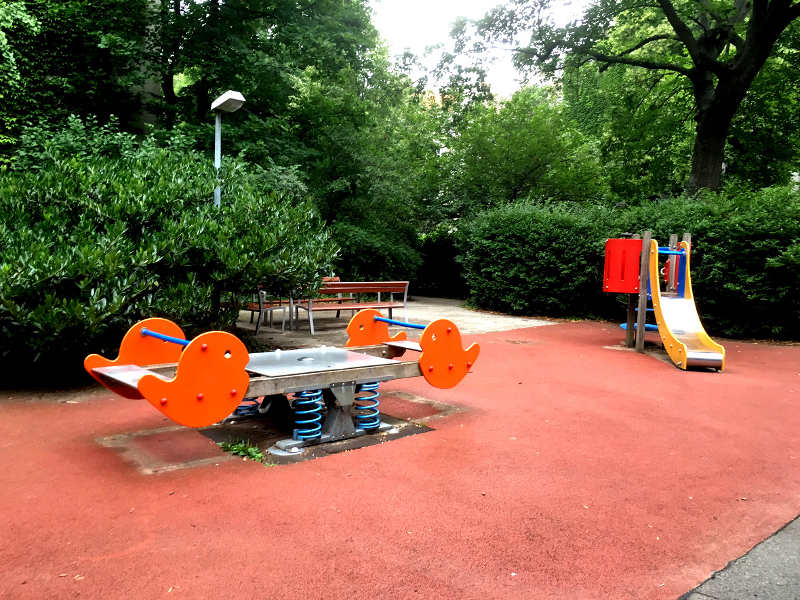 Wippe und Kleinkindrutsche auf Fallschutzboden vor Sträuchern