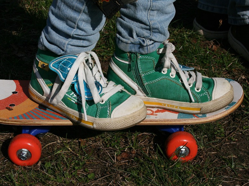 Ein Kind mit grünen Turnschuhen steht auf einem bunten Kinderskateboard