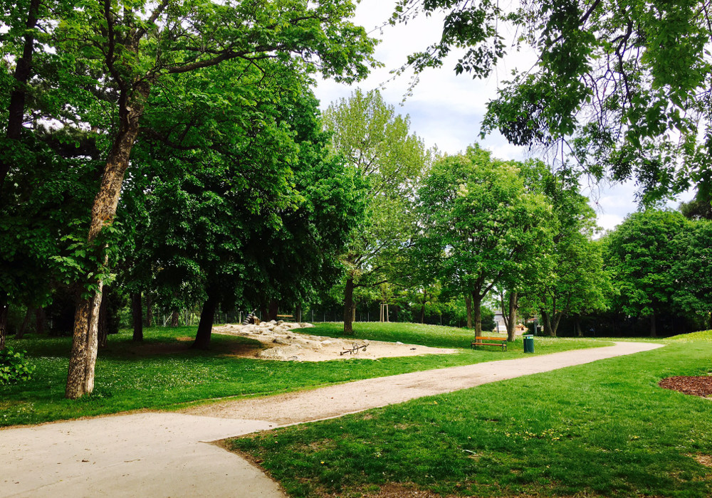 Park mit Weg und kleinem Sandspielbereich.