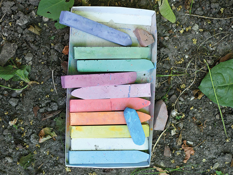 Schachtel mit bunter Kreide steht auf Erdboden