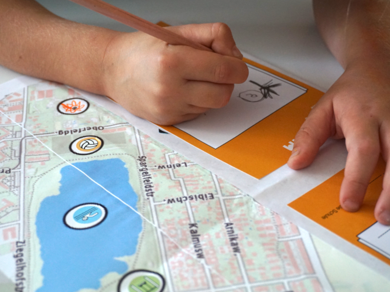 Kinderhand mit Buntstift zeichnet auf persönlich gestaltetem Grätzlplan