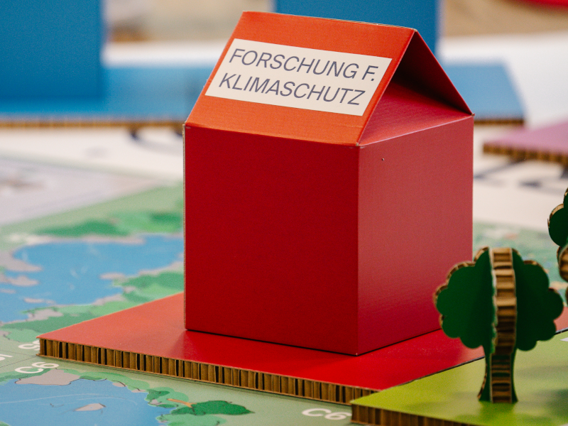 Rotes Häuschen auf Spieluntergrund mit Beschriftung "Forschung für Klimaschutz"