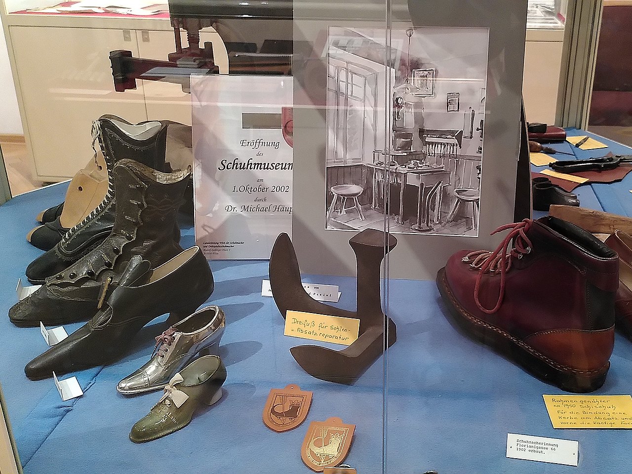 Schaukasten mit diversen handgefertigten Schuhen aus dem 20. Jahrhundert sowie ein Dreifuß für Sohlen- und Absatzreparatur. 