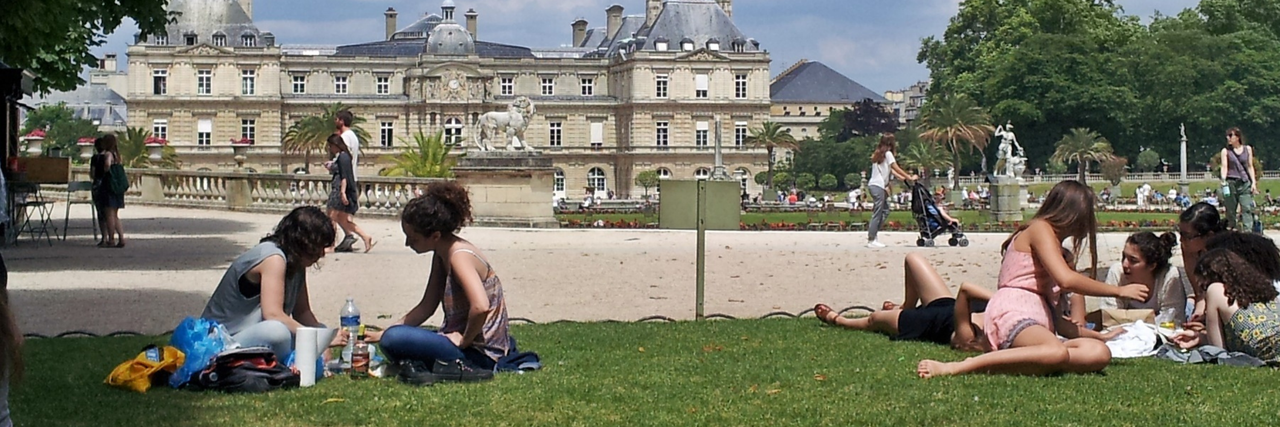 zwei Gruppen Jugendlicher sitzen nebeneinander in einem Park. Im Hintergrund ist ein Schloss