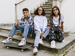 Drei Jugendliche sitzen auf einer Stiege.