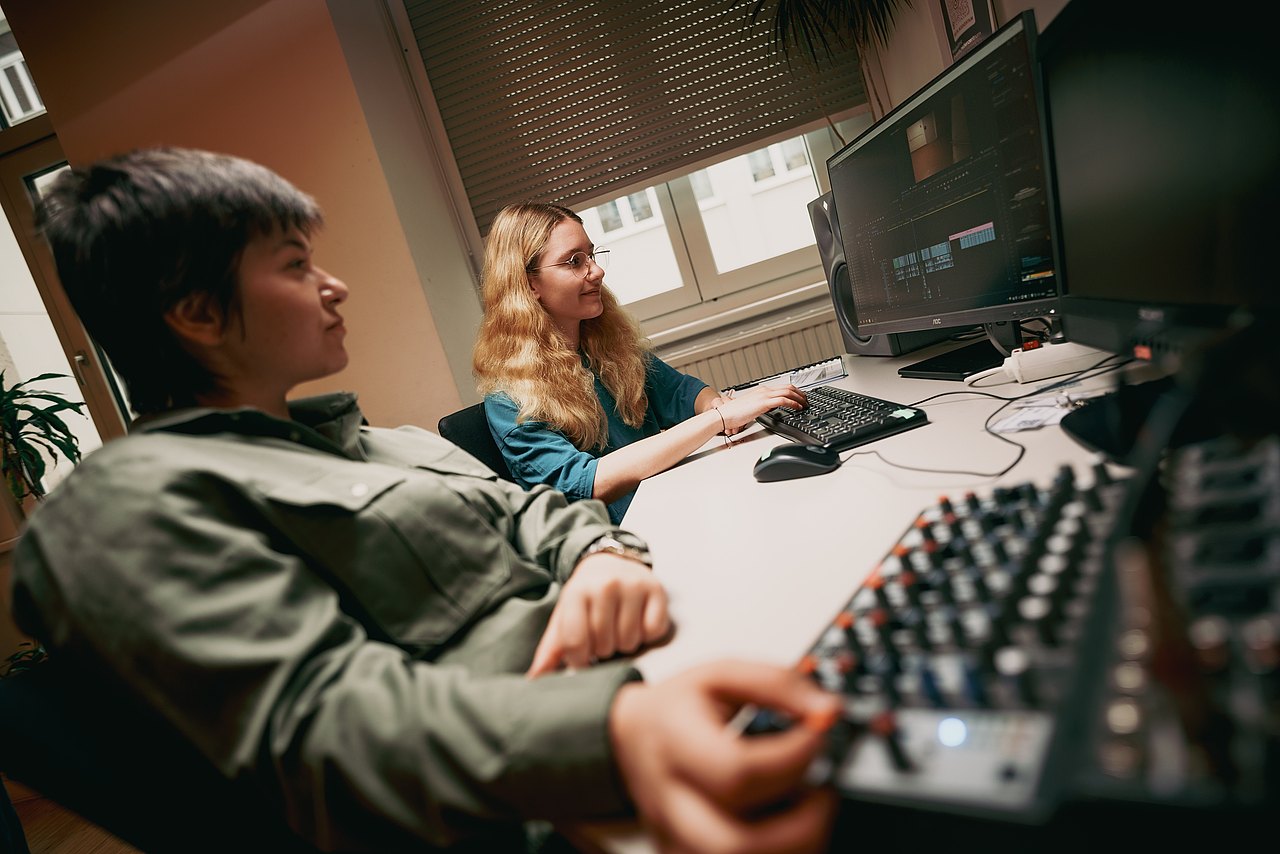 zwei Frauen sitzen vor einem Computer, auf dem ein Videoschnittprogramm geöffnet ist