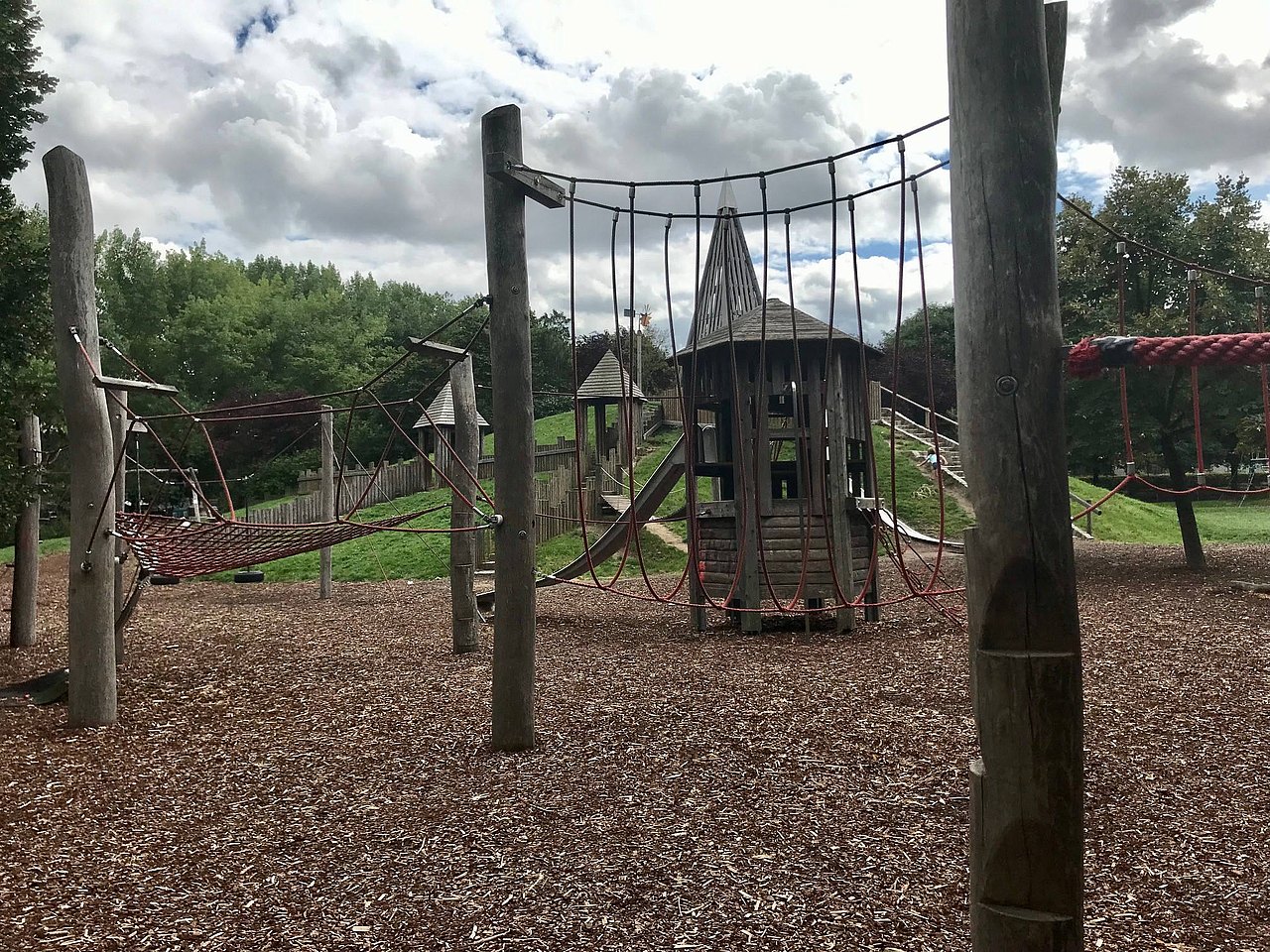 Kletterparkour aus mehreren Holzpfeilern, zwischen denen rote Seile auf verschiedene Weisen gespannt sind.