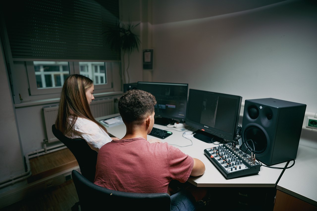 Zwei Jugendliche erstellen einen Filmschnitt vor zwei Computermonitoren.